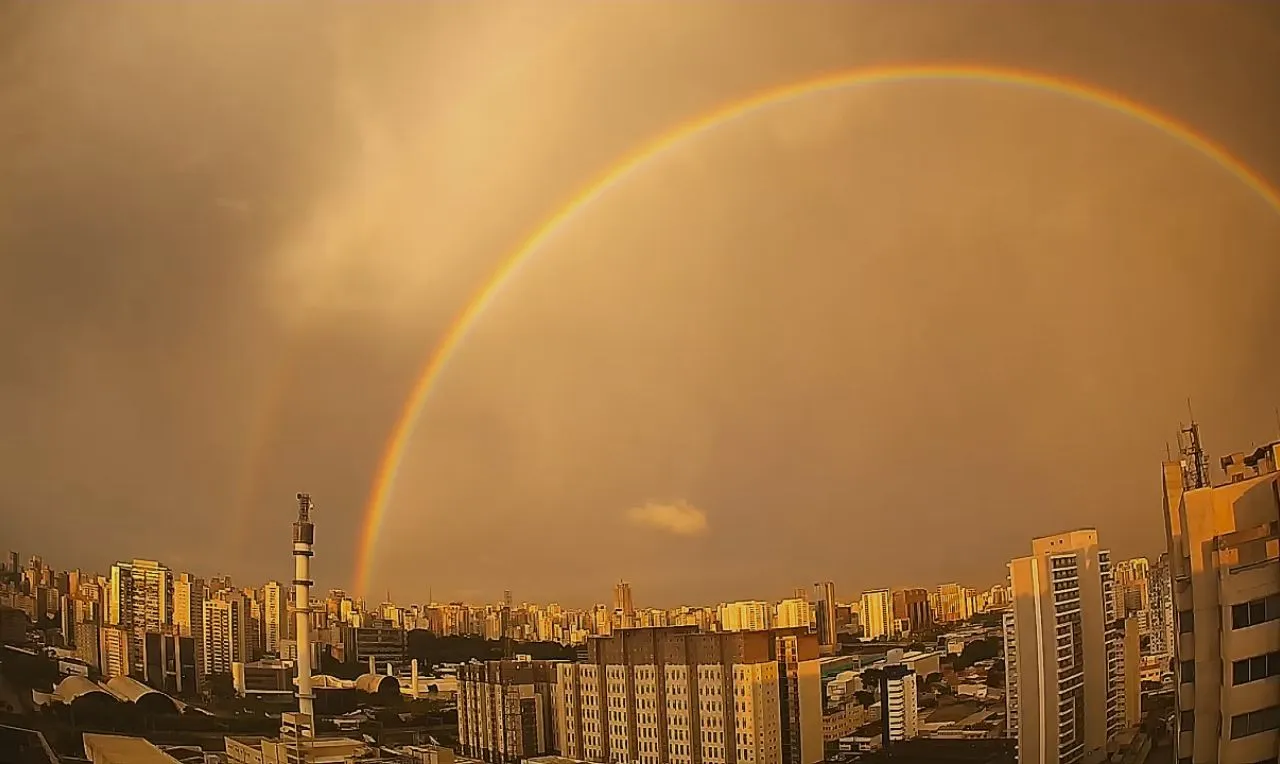 a imagem mostra a forma&ccedil;&atilde;o de chuva e um arco-&iacute;ris na capital paulista